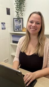 junge Frau sitzt an ihrem Schreibtisch vor ihrem Laptop und lächelt in die Kamera